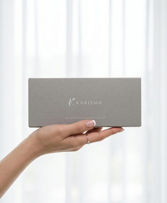 一隻手溫柔捧著 KARISMA 自若 Discovery Set 香氛探索禮盒，灰色的極簡質感包裝內含 10 款天然花精香氛噴霧，是送禮與情緒療癒的首選。